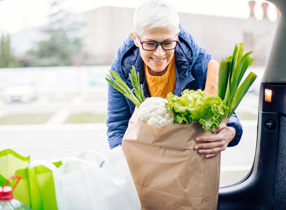 A woman with groceries in a paper bag in the back seat of a car.