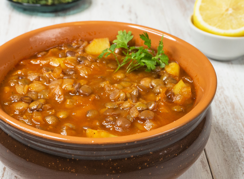 A bowl of lentil soup on a table next to a lemon.