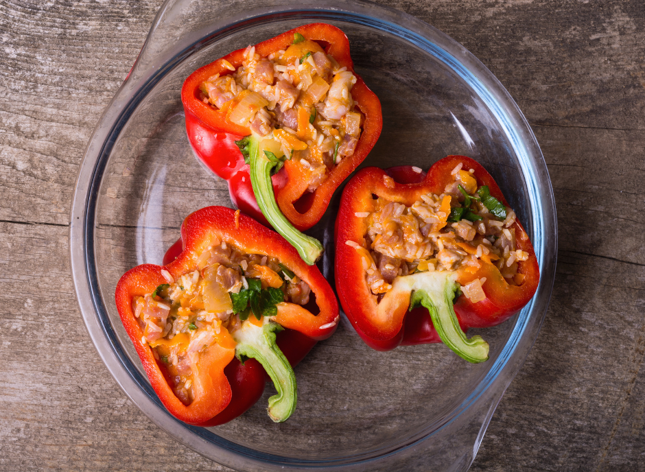 Three stuffed peppers in a glass dish on a wooden table.
