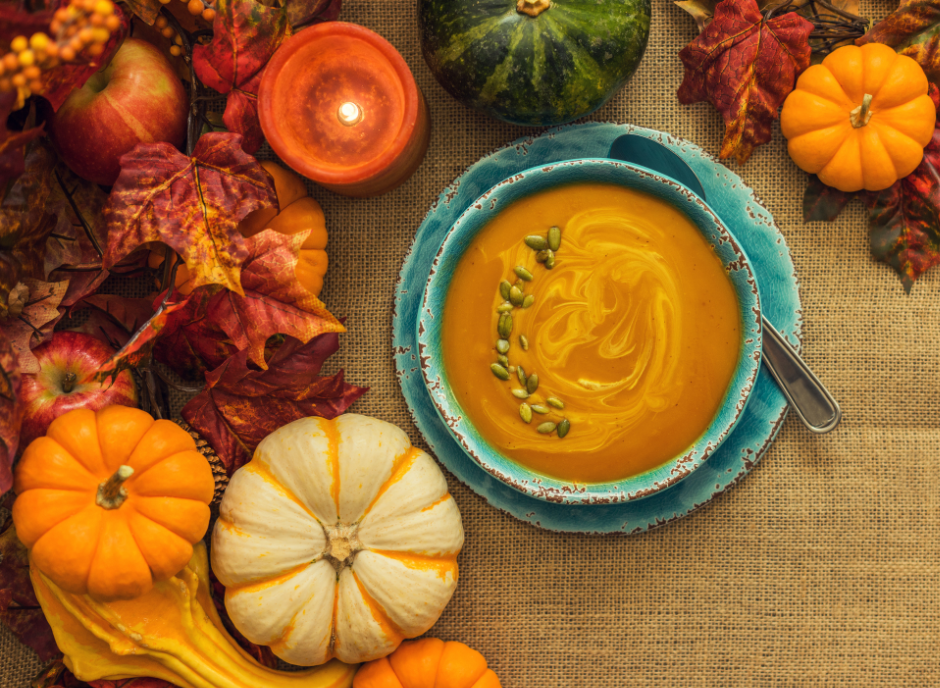 A bowl of pumpkin soup surrounded by pumpkins and candles.