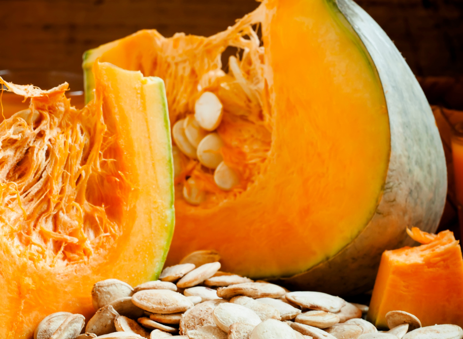 A pumpkin is cut in half and surrounded by pumpkin seeds.