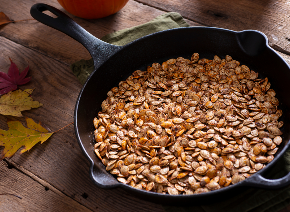 A skillet filled with pumpkin seeds on a wooden table.