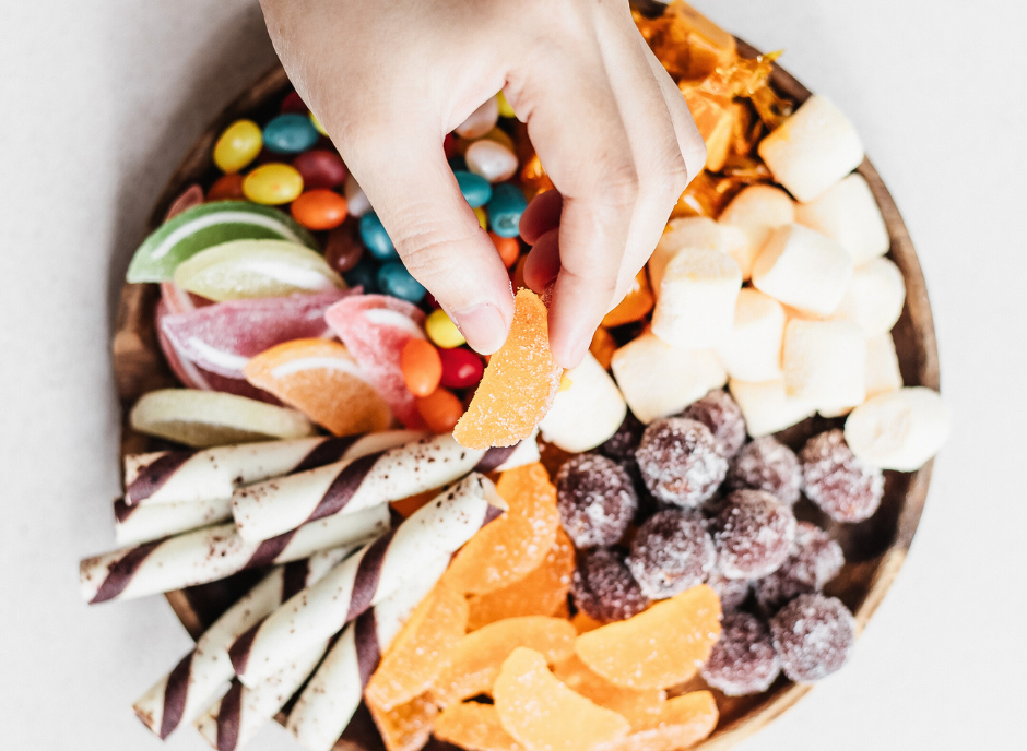 A hand is holding a plate full of different kinds of candy.