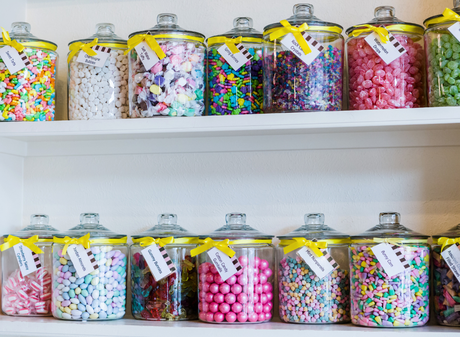 Many candy jars are lined up on a shelf.
