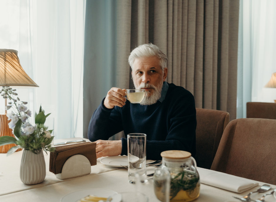 A bearded man enjoying a cup of tea at a table in a restaurant.