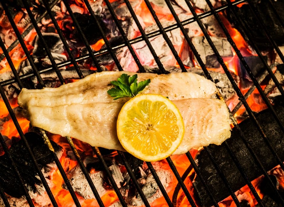 A fish fillet on a grill with a lemon slice.