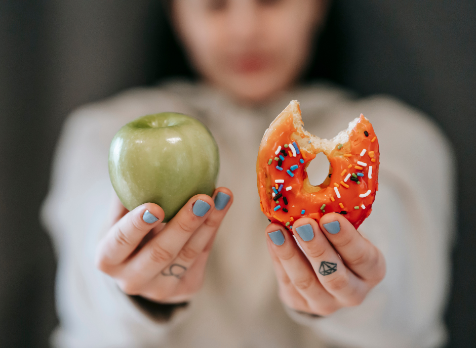 A woman holding an apple and a donut.