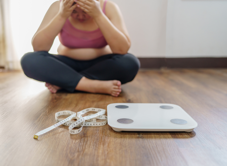 A woman sits on the floor next to a weight scale.