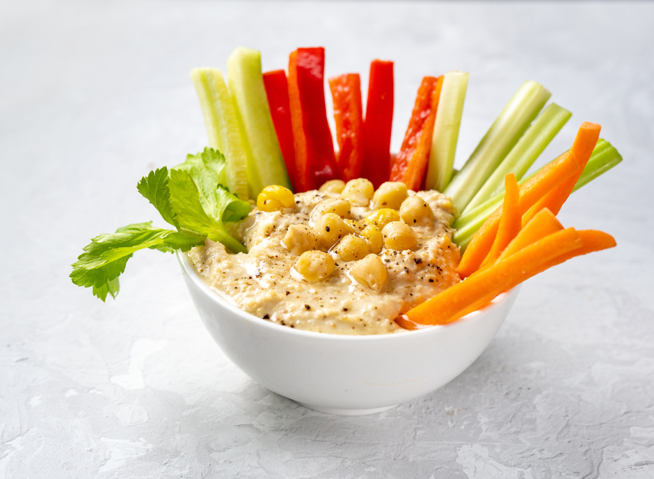 A bowl of hummus with carrots, celery and chickpeas.