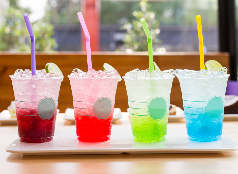 Four colorful drinks on a tray with straws.