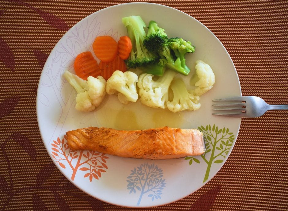 A plate with a piece of fish and vegetables on it.