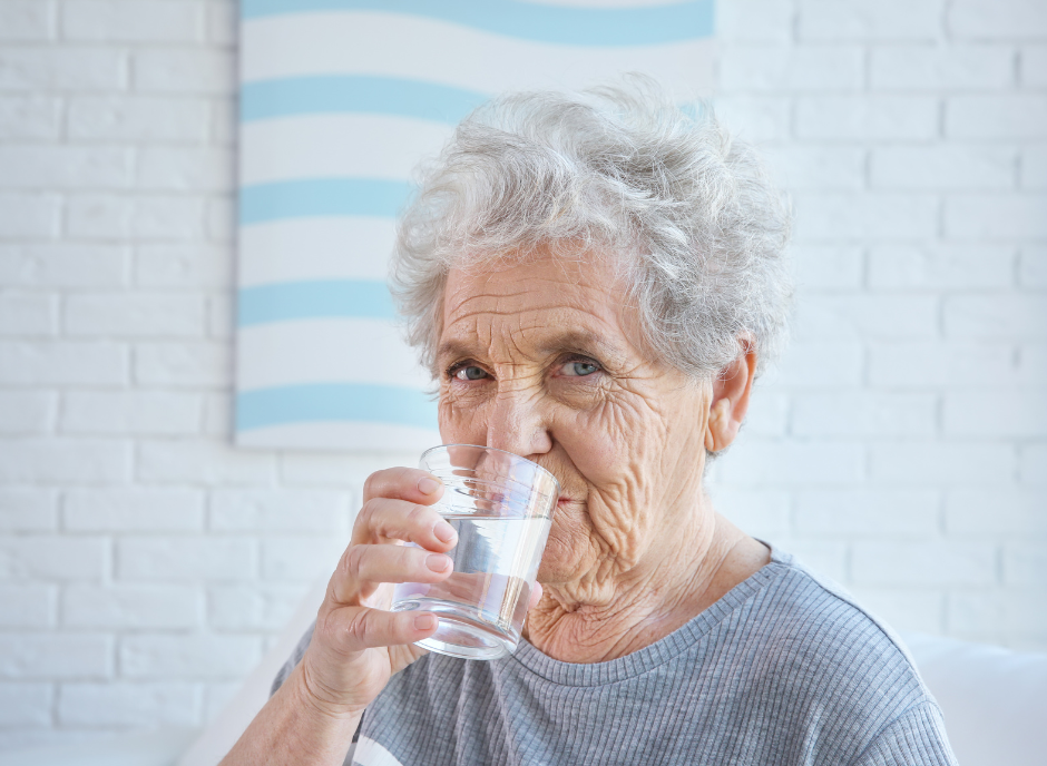 An elderly woman drinking water from a glass.