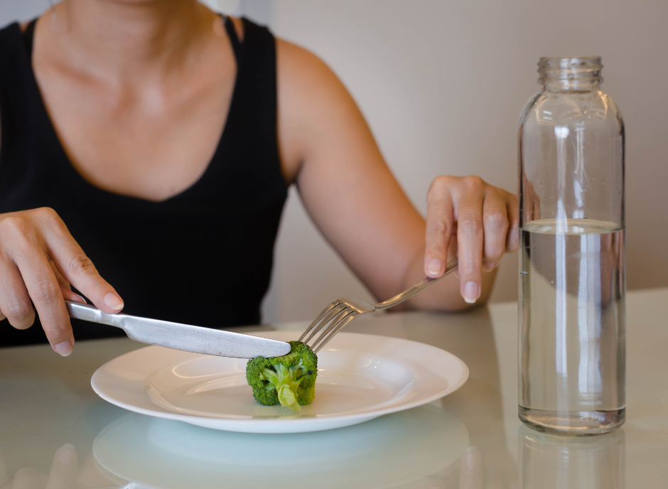 A woman is eating a plate of broccoli with a fork and knife.