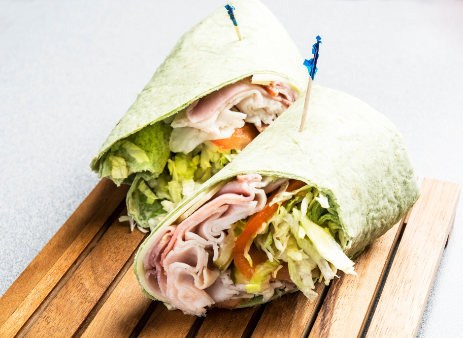 A wrap with ham and lettuce on a wooden board.