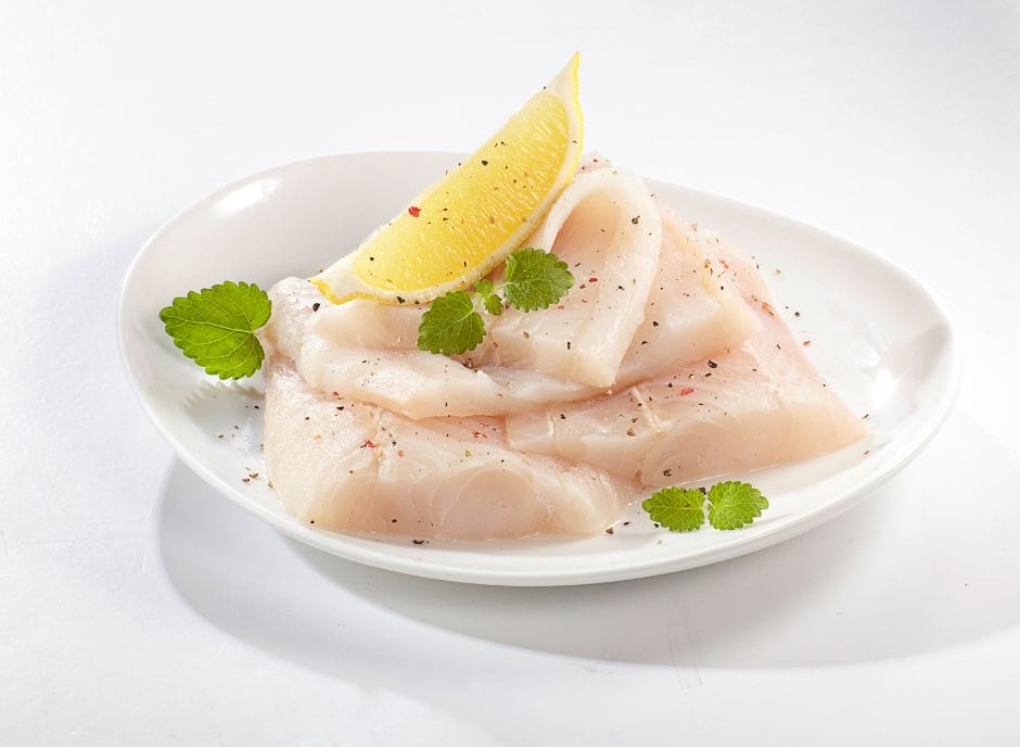 Fresh tuna fillet on a white plate with a lemon slice.