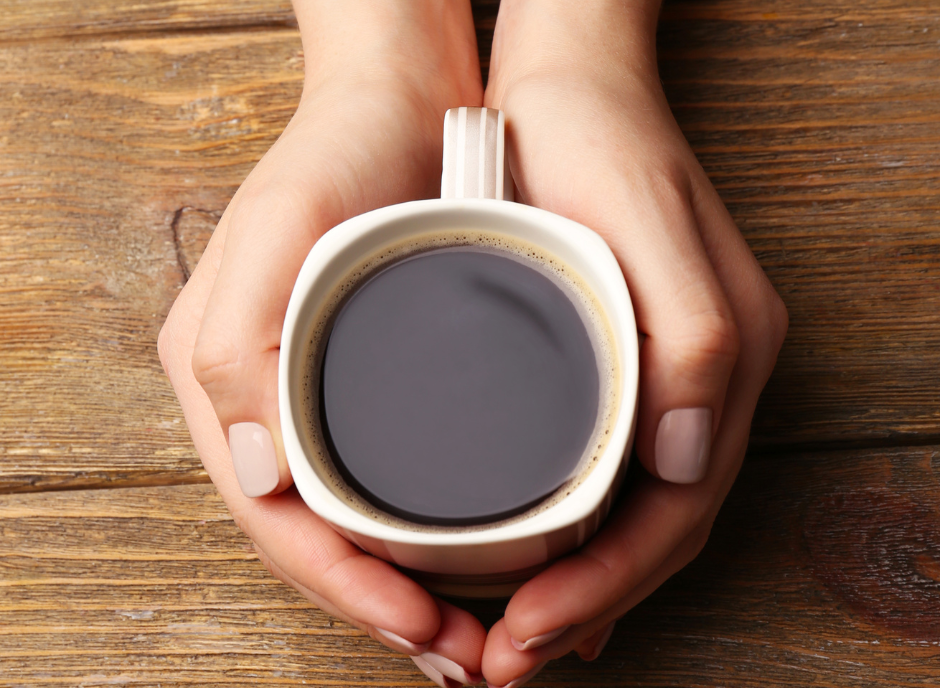 A woman's hands holding a cup of coffee on a wooden table.