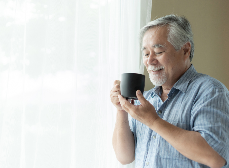 Senior asian man holding a coffee mug in front of a window.