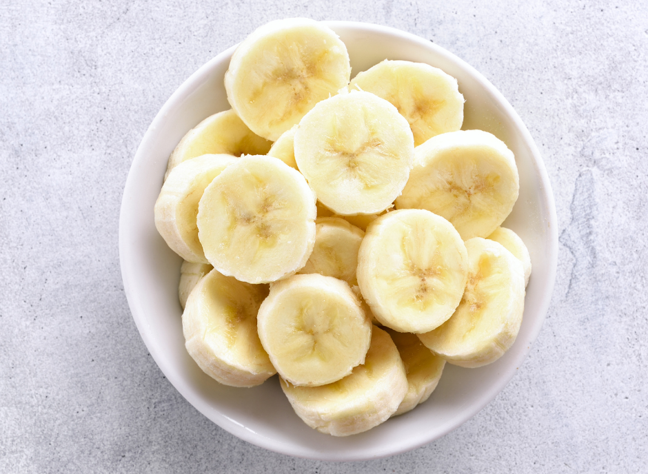 Sliced bananas in a white bowl on a gray background.