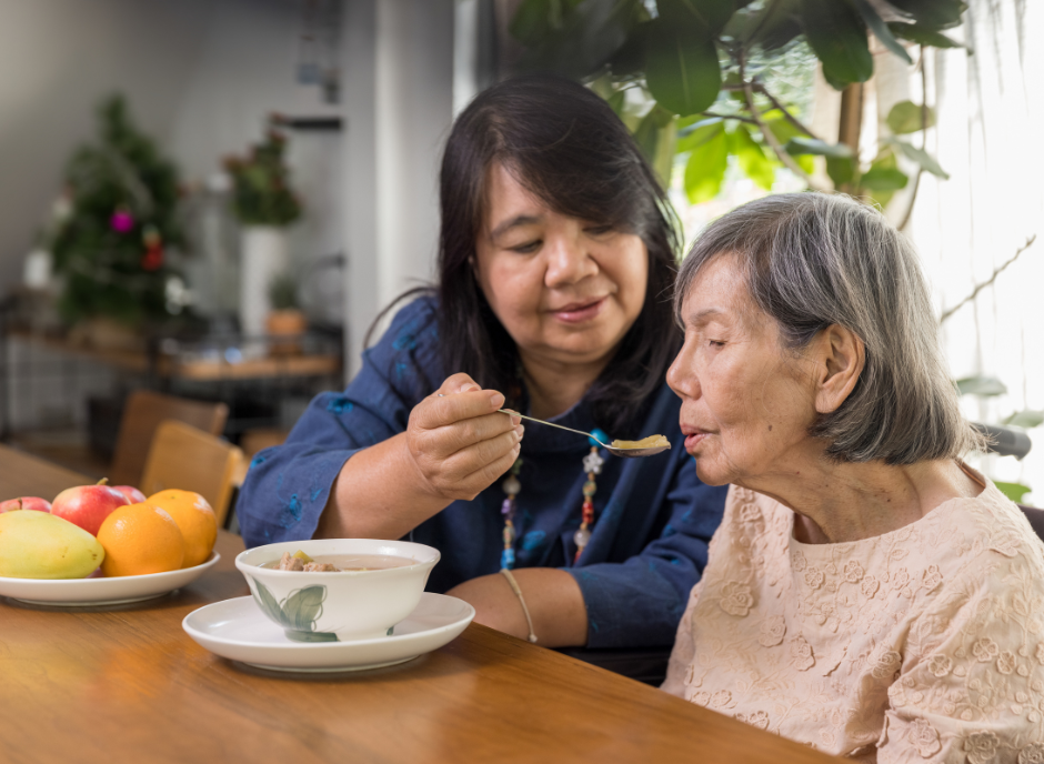 A woman is helping an elderly woman eat a bowl of cereal.