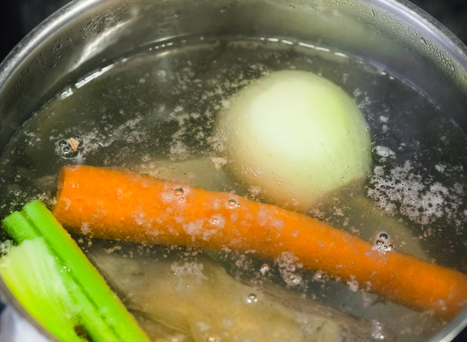 A pot with carrots, celery and onions in it.