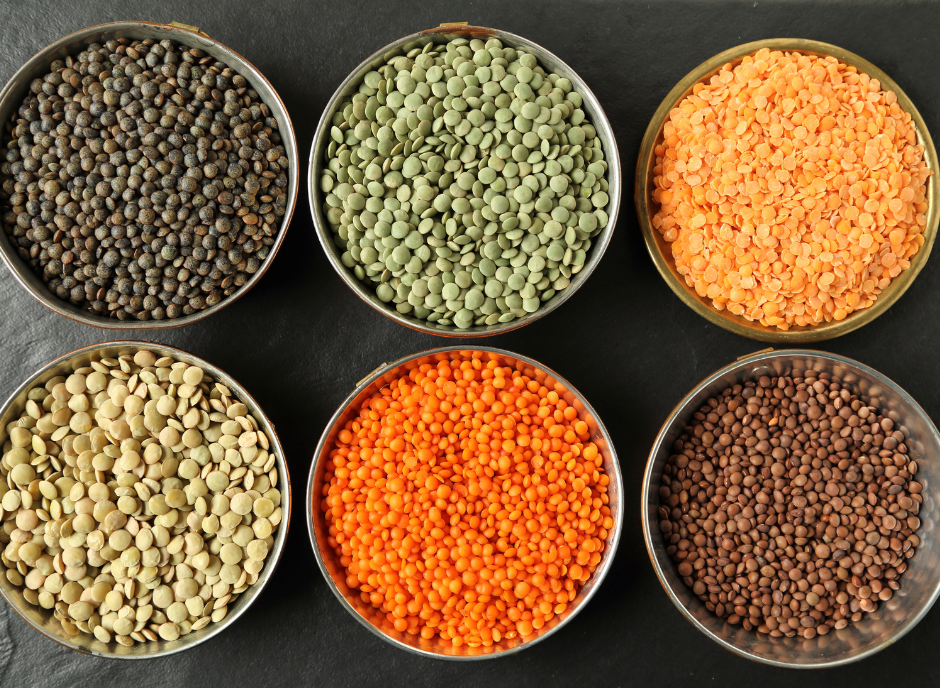 Varieties of lentils displayed in bowls on a black surface.