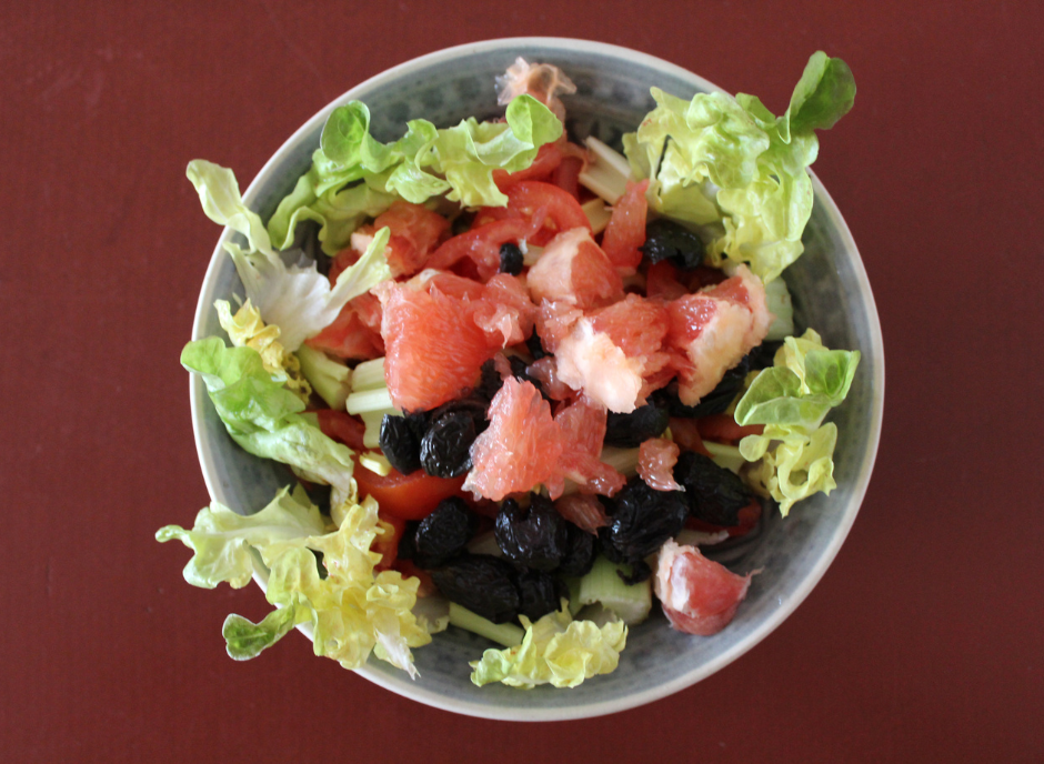 A bowl of salad with grapefruit, black olives and lettuce.