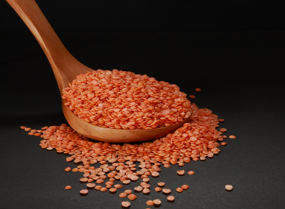 A spoon full of red lentils on a black background, suitable for kidney disease.