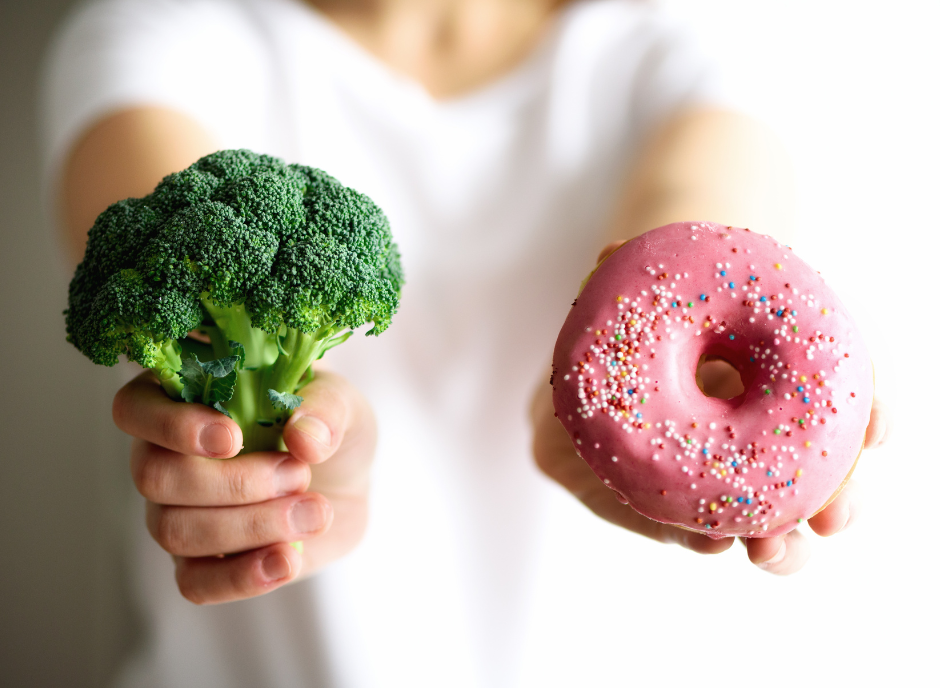 A woman holding a donut and broccoli, showcasing her choice between indulgence and maintaining a kidney-healthy diet.