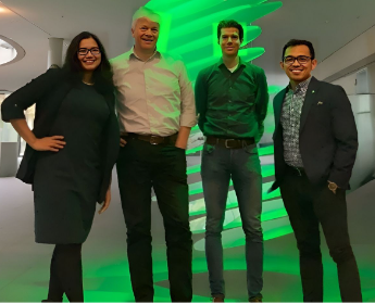 Four professionals standing side by side, smiling in front of a green illuminated feature.