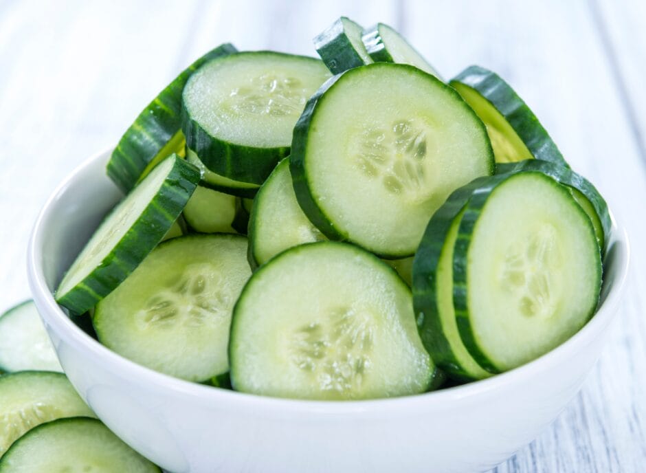 A bowl of sliced cucumbers on a wooden table.