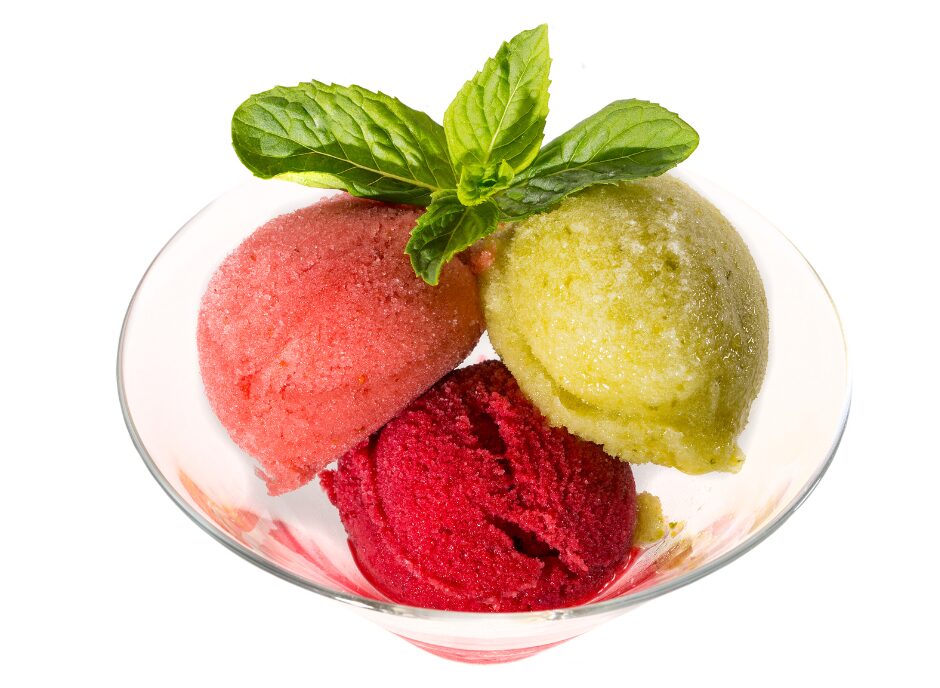 A glass bowl containing three scoops of sorbet in different colors: red, green, and pink, garnished with a sprig of mint on top.