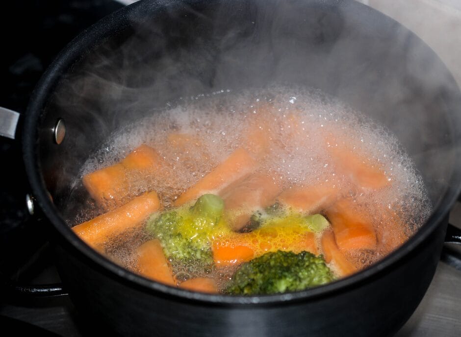 Carrots and broccoli boiling in a black pot with bubbling water.