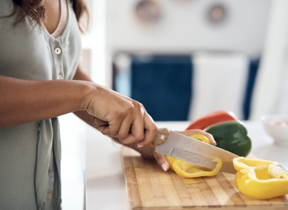 A person slices a yellow bell pepper on a wooden cutting board in a kitchen.