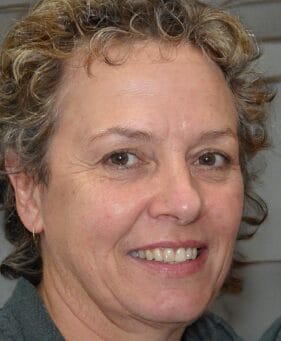 Close-up of a smiling person with short curly hair, looking into the camera.